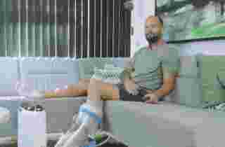 Mann sitzt entspannt auf dem Sofa und wendet währenddessen die FlowOx™ Therapie am Bein an
